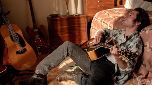 Jeremy Allen White as Bruce Springsteen on the floor playing the guitar.