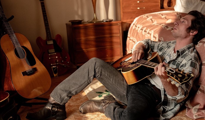 Jeremy Allen White as Bruce Springsteen on the floor playing the guitar.