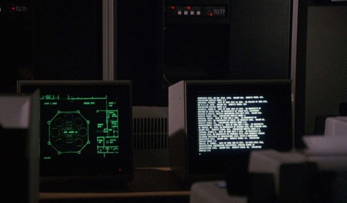 Some old computers from the movie Wargames. One with a green-on-black screen and some schematics; the other with a white-on-black prompt.